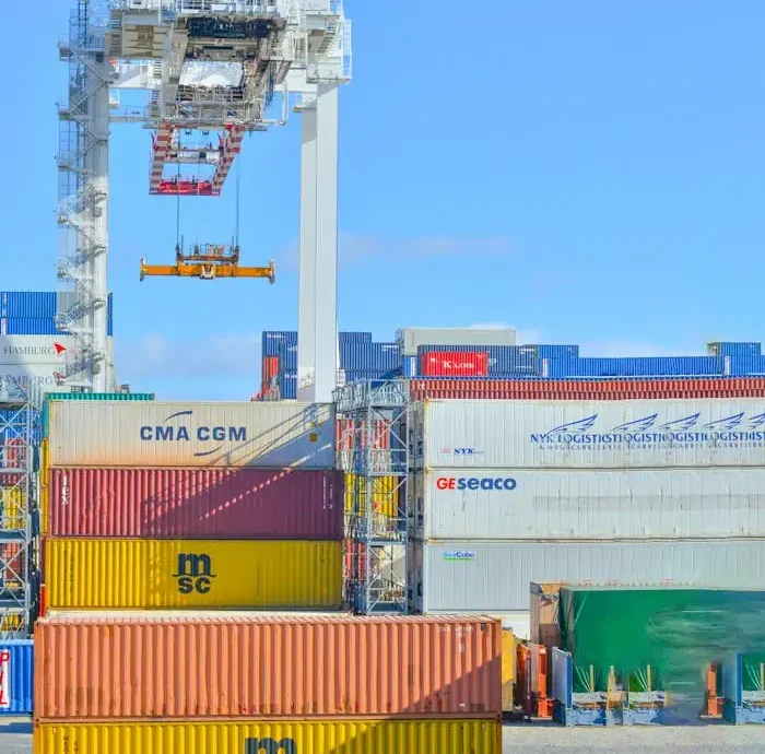 Stacked cargo containers in a sunny port industrial setting with crane.